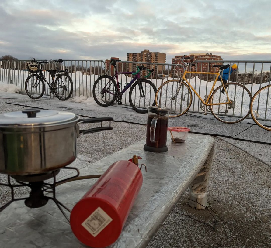 Several bikes lined up along a fence in the background with a port and french press in the foreground. 